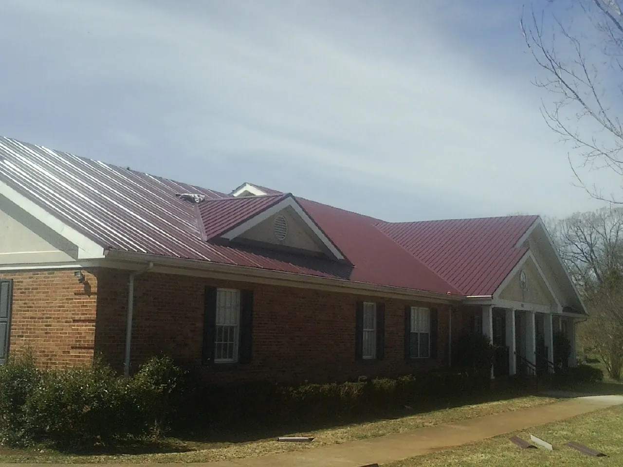 Red metal roof with gabled entries on a long brick building, from a Hail Damage Roof Repair job in Ruthton