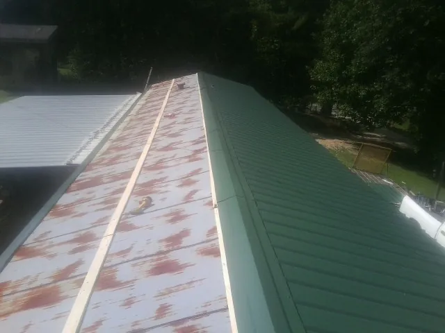 Old rusted panels beside newly installed green metal roofing — Wind Damage Roof Repair by Roofing Brothers in Ruthton