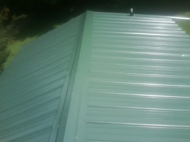 New green metal panels meeting at the ridge of a roof — Flat Roof Repair work by our crew in Ruthton