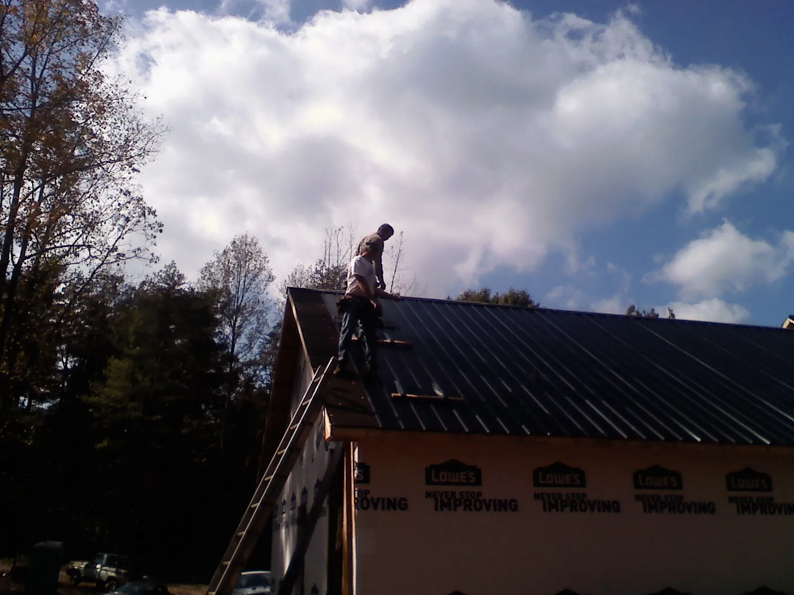 Roofer fastening dark metal panels high against a cloudy sky, from a Roof Inspection job in Ruthton