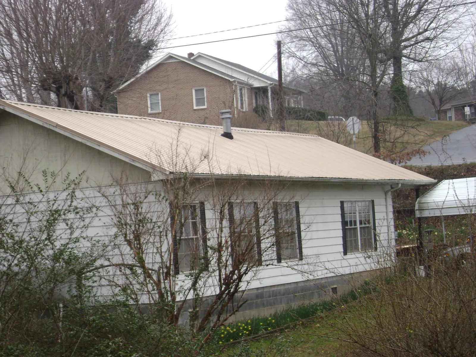 Tan metal roof on a white sided house set into a hillside — Commercial Roofing by Roofing Brothers in Ruthton